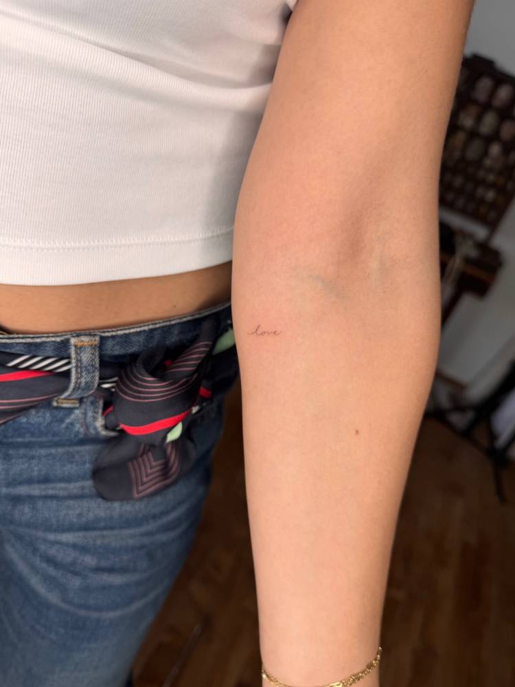 Tiny tattoo of the word "love" in handwritten font.