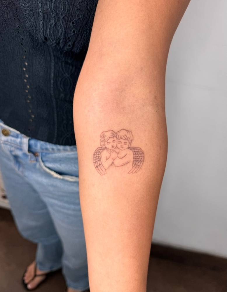 Fine line style cherubs tattoo located on the inner forearm.