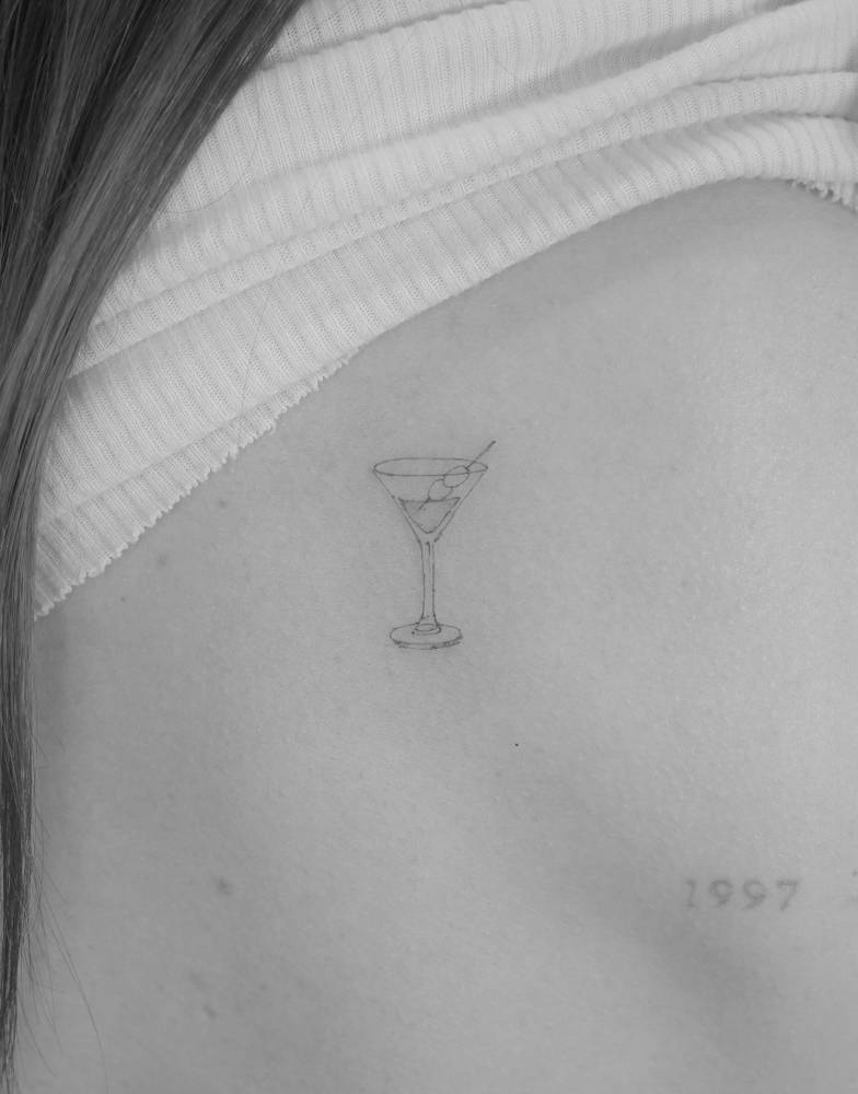Fine line style Martini cocktail tattoo placed on the shoulder blade.