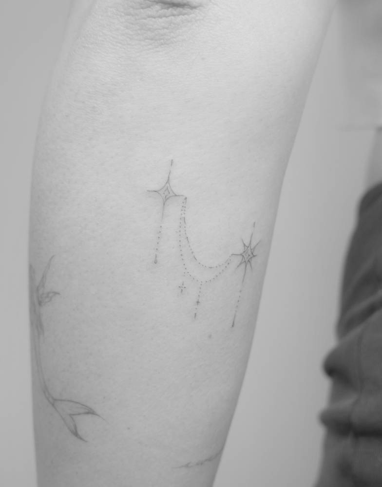 Ornamental stars tattoo in fine line style located on the forearm.