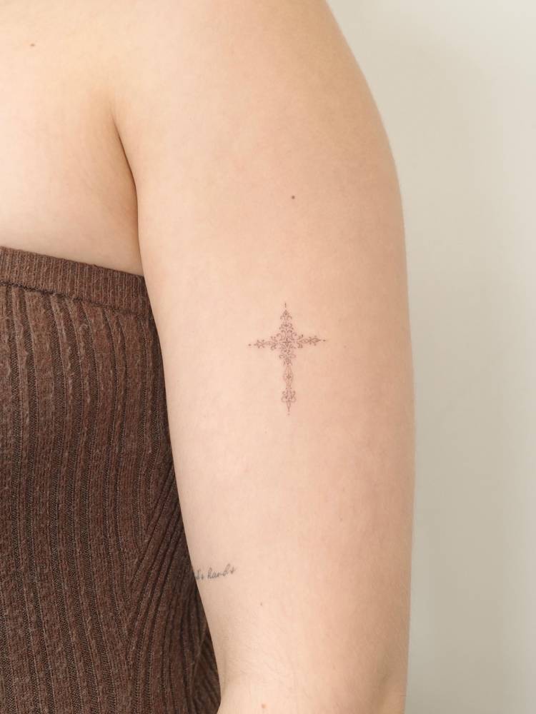 FIne line style ornamental cross tattooed on the upper arm.