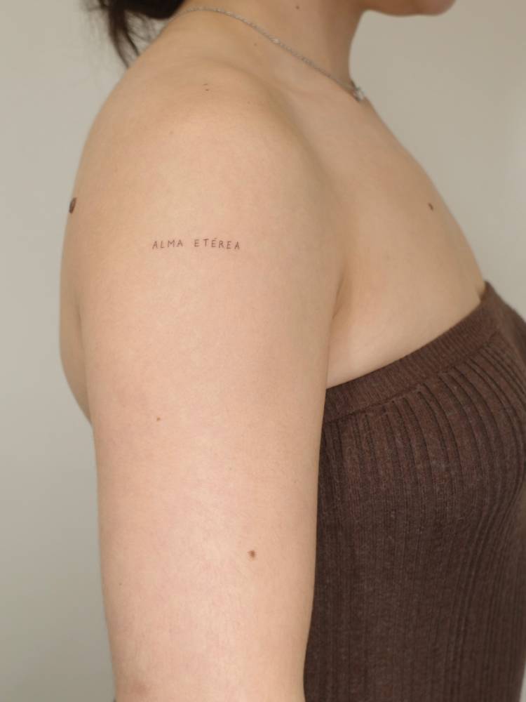 "Alma etérea" lettering tattoo located on the upper arm.