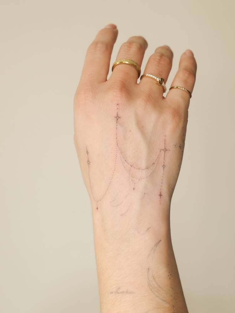 Ornamental design tattooed on the hand, done in fine line style.