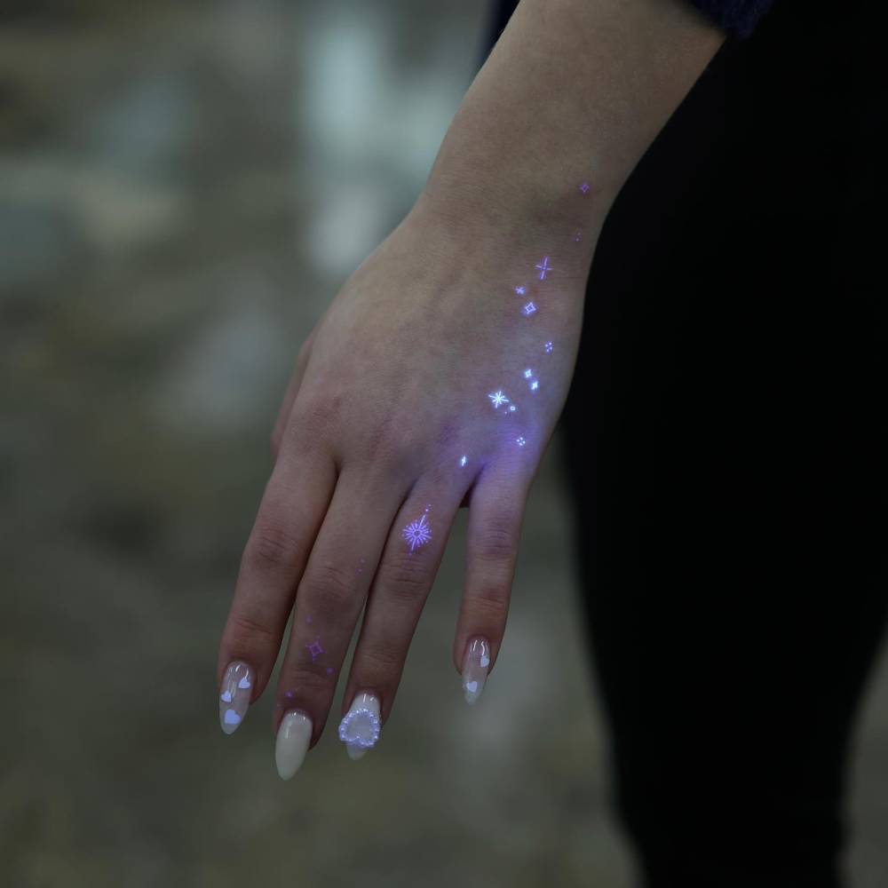 Sparkling stars tattoo in UV ink located on the hand.