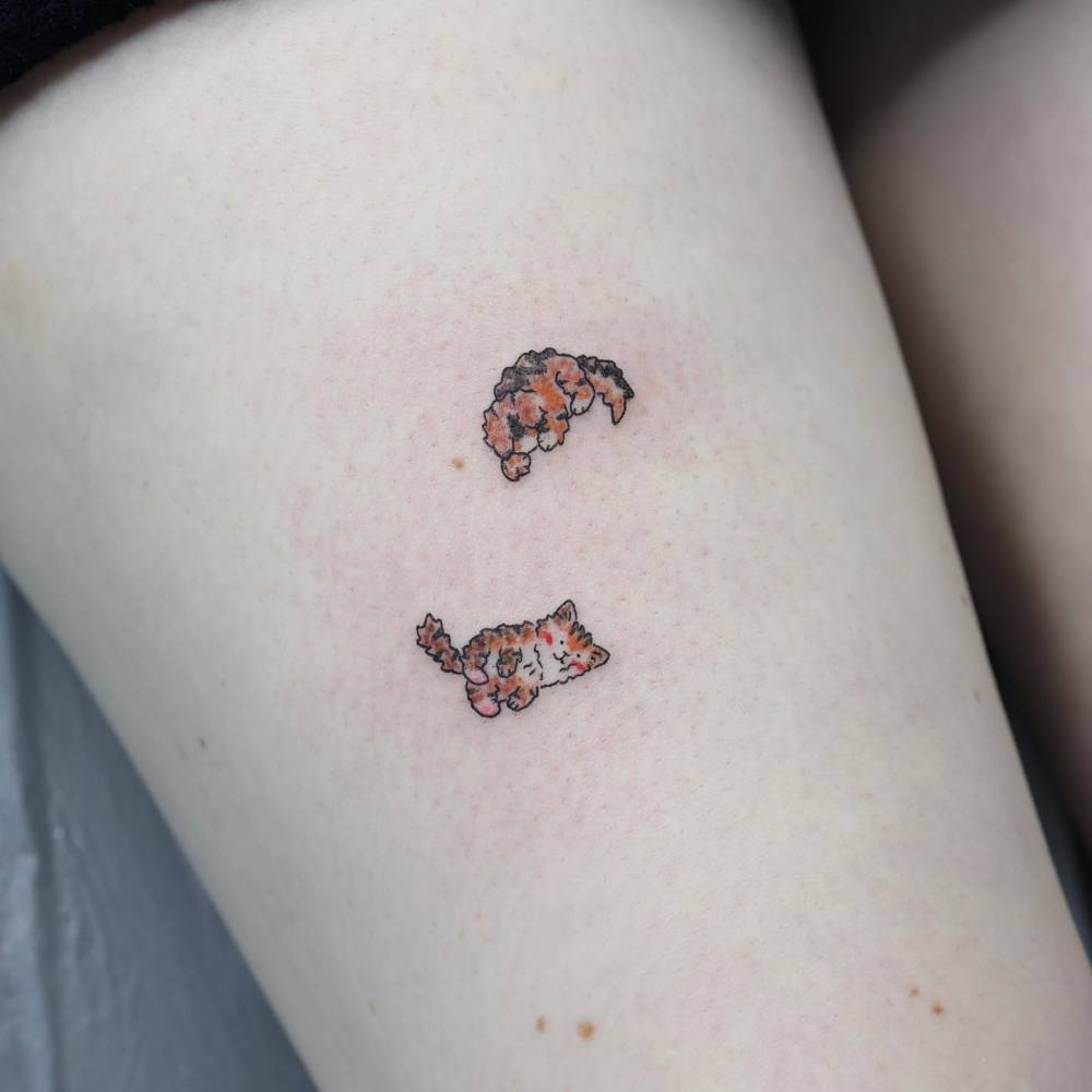Cartoon style cat and dog tattoo located on the thigh.