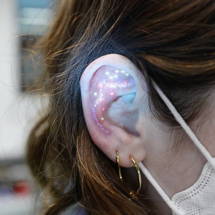 UV ink galaxy tattoo in minimalistic style located on the ear.
