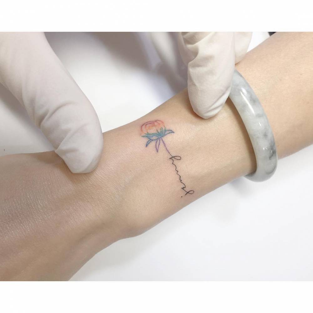 Spectrum rose and name "Jenny" tattooed on the wrist.