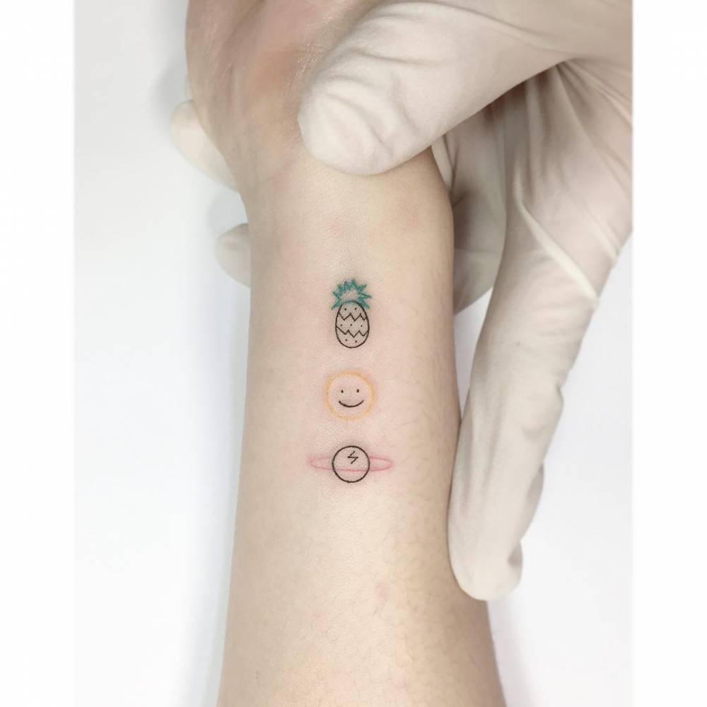 Pineapple, smiley and Saturn tattoo in minimalistic style located on the wrist.