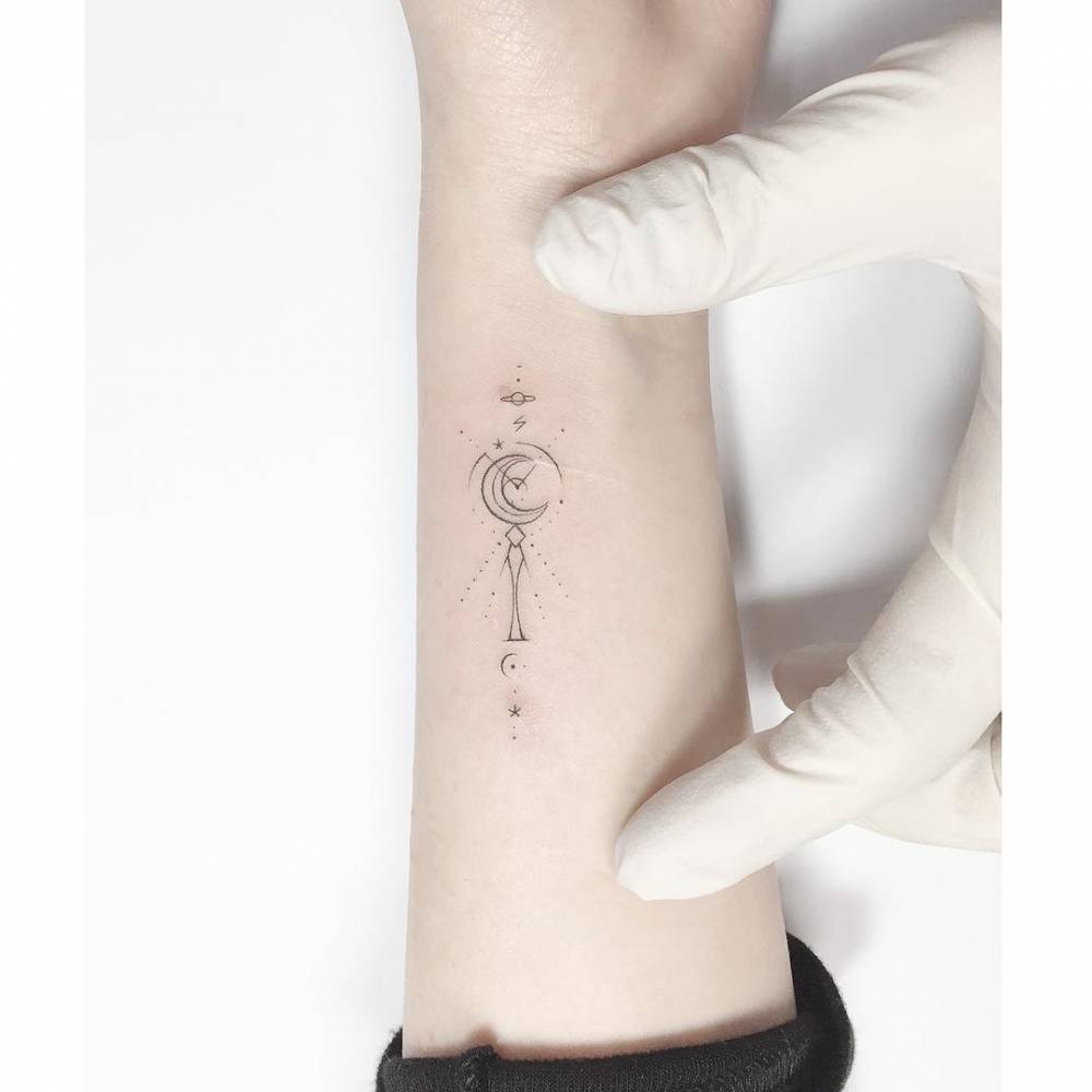 Moon Stick tattoo in fine line style placed on the wrist.