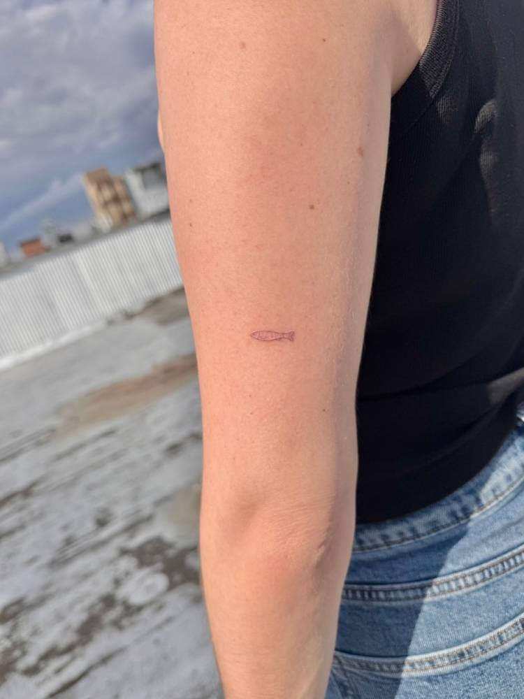 Tiny sardine tattoo located on the tricep, done in fine line style.