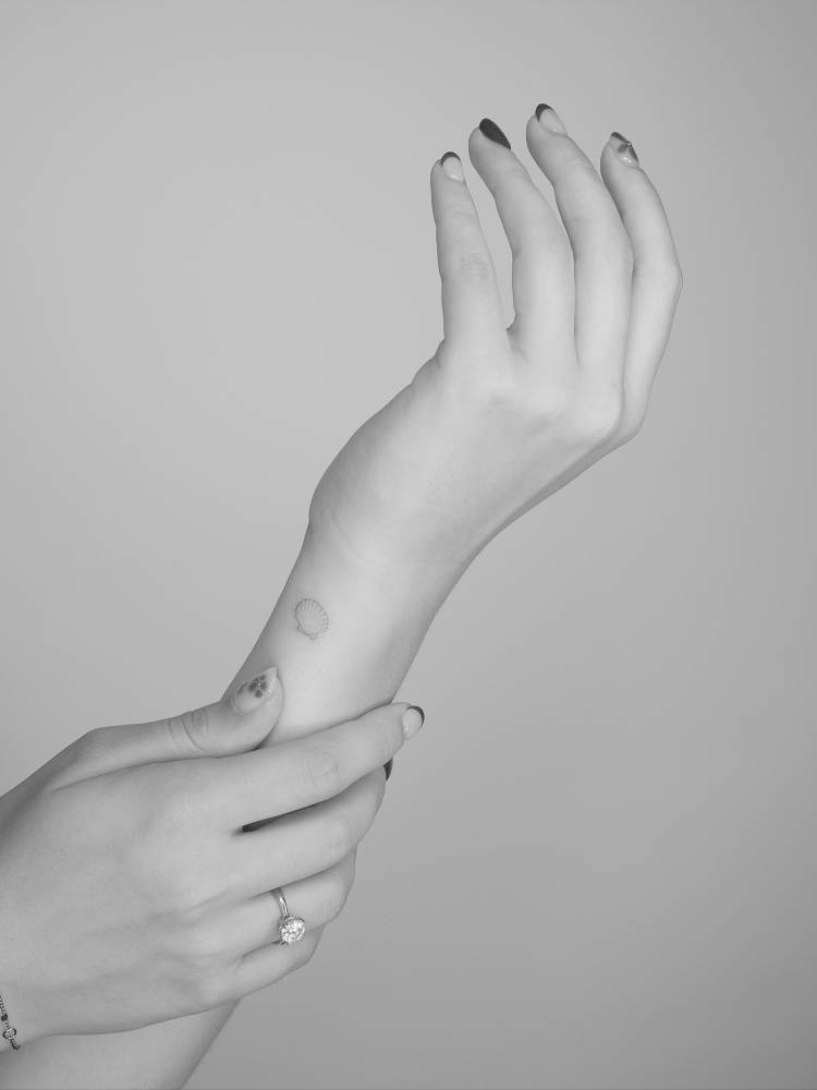 Fine line style scallop shell tattoo located on the wrist.