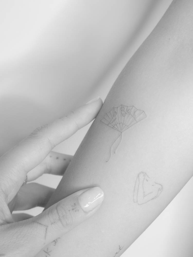 Hand fan tattoo located on the inner forearm, fine line style.