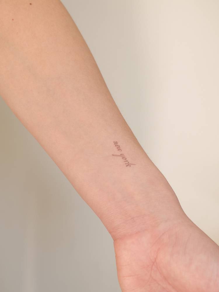 Script font "New York" lettering tattoo located on the wrist.
