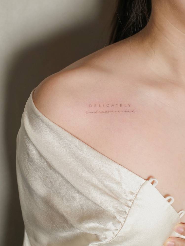 "Delicately interconnected" lettering tattoo located on the collarbone.