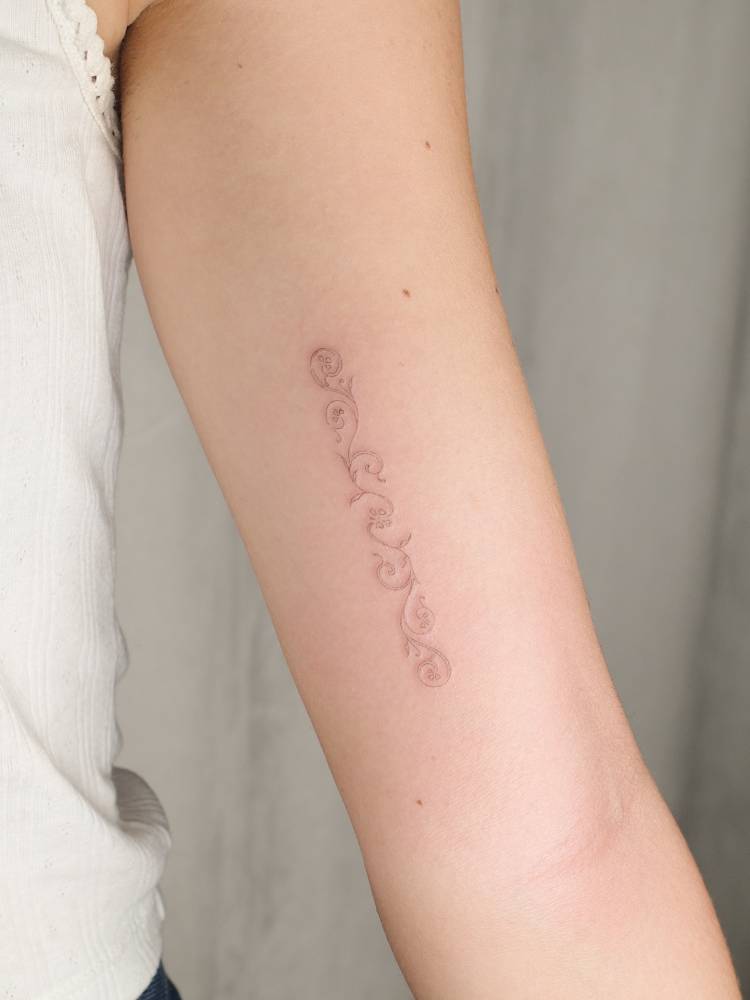 Fine line style ornamental flowers tattooed on the inner arm.