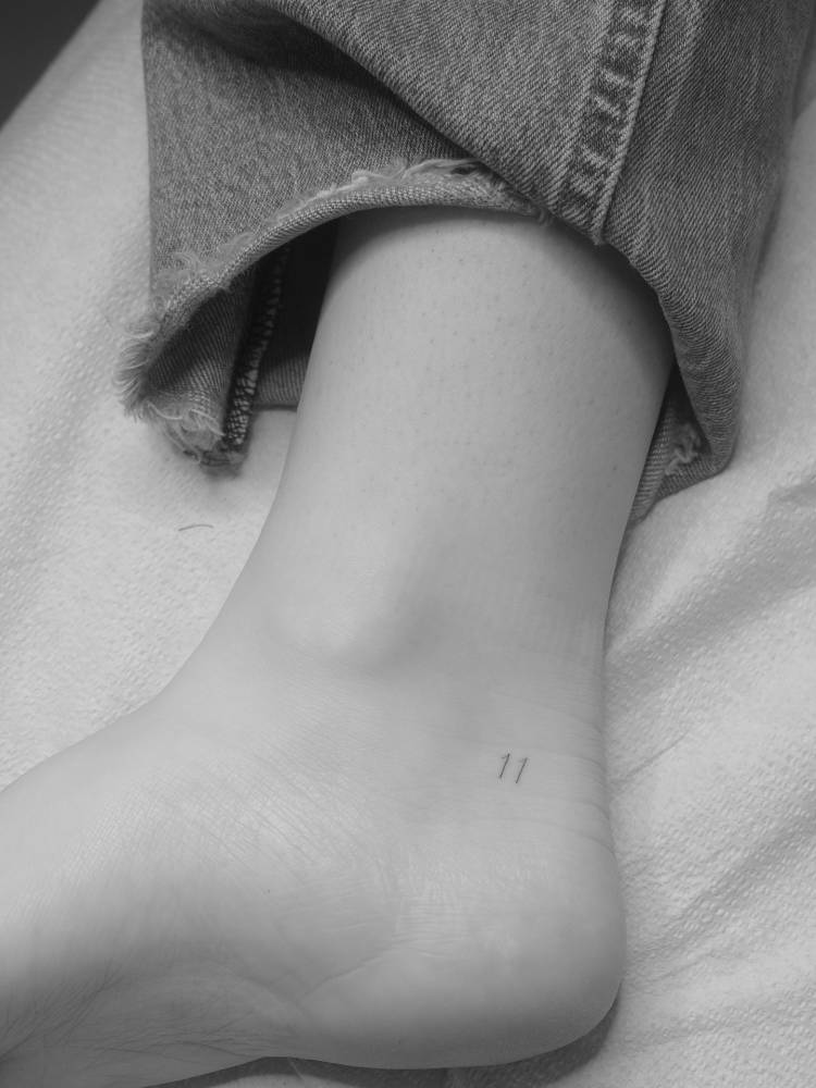 Tiny minimalist tattoo of the number "11" placed on the ankle.