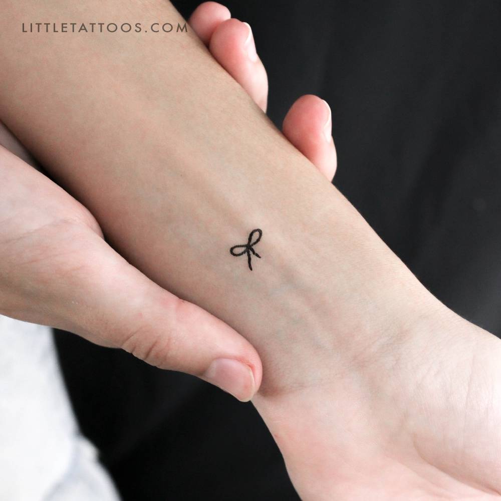 Tiny bow temporary tattoo located on the wrist.