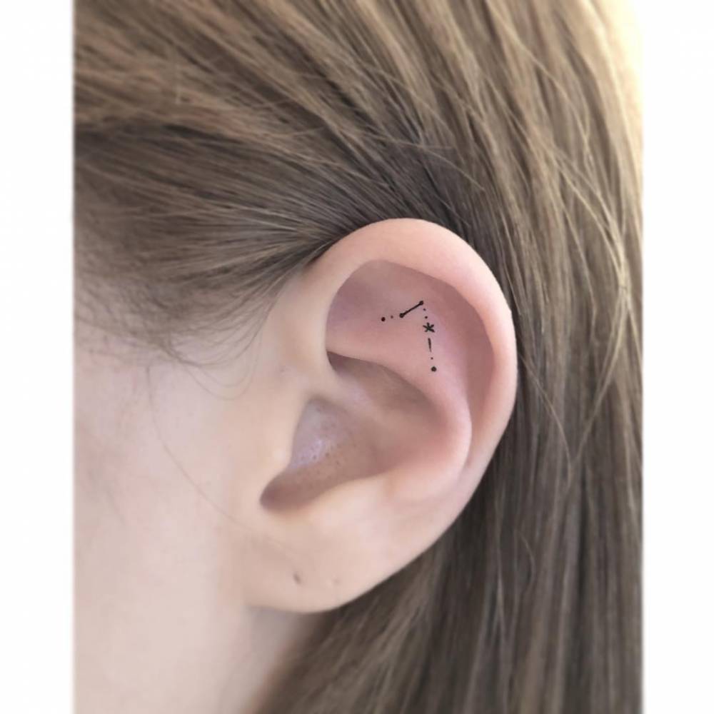 Tiny Pisces constellation tattooed on the ear, minimalist style.