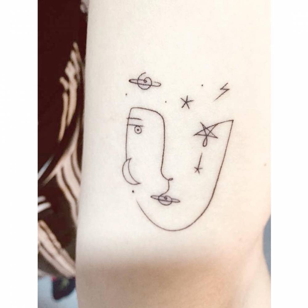 Face and universe tattoo located on the wrist, done in minimalist style.