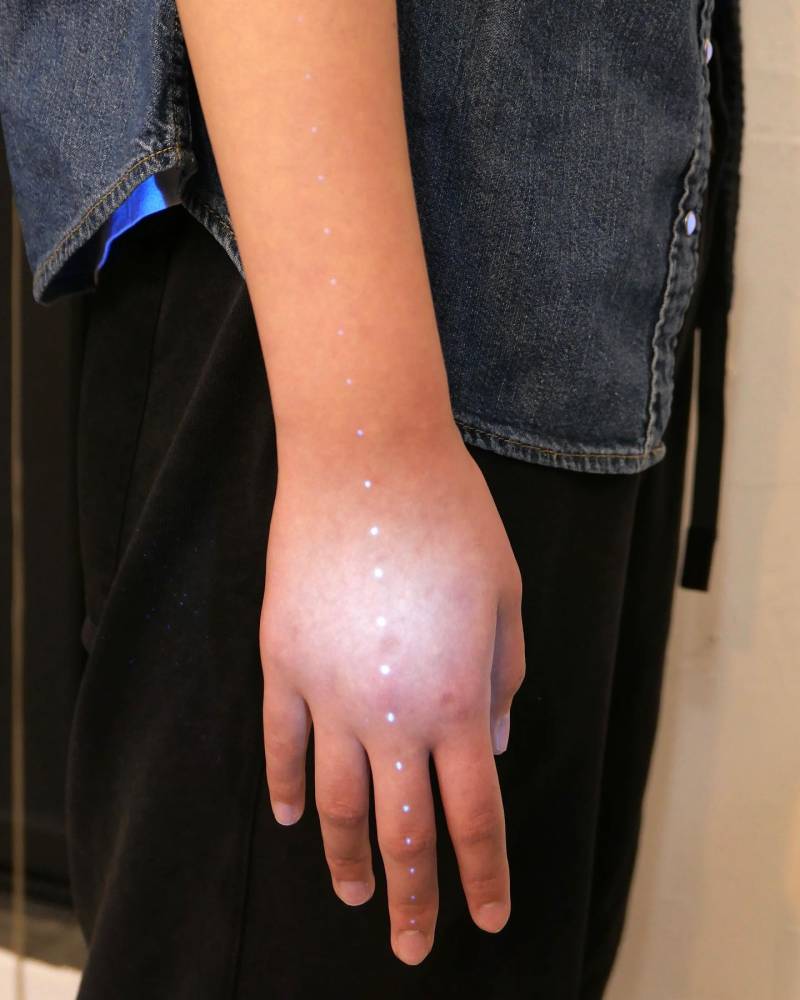 UV ink dots tattoo located on the hand and forearm.