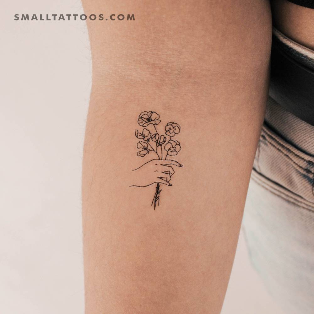 Small hand holding flowers temporary tattoo located on the inner forearm.