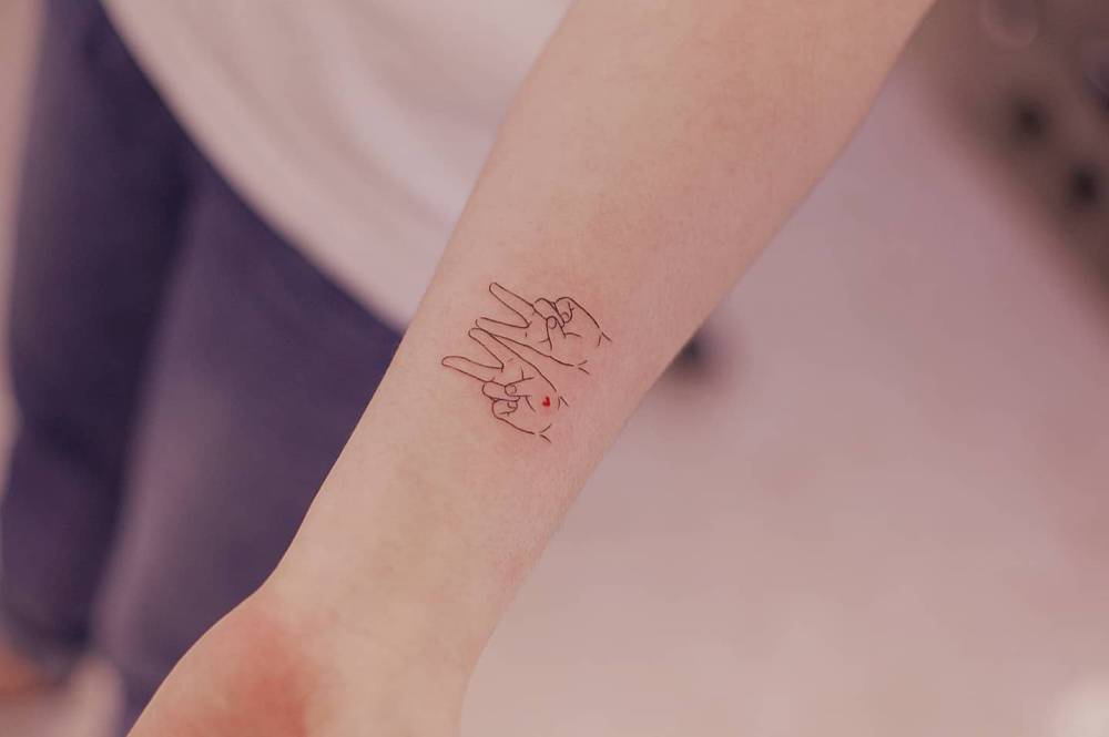V sign tattoo located on the wrist, done in fine line style.