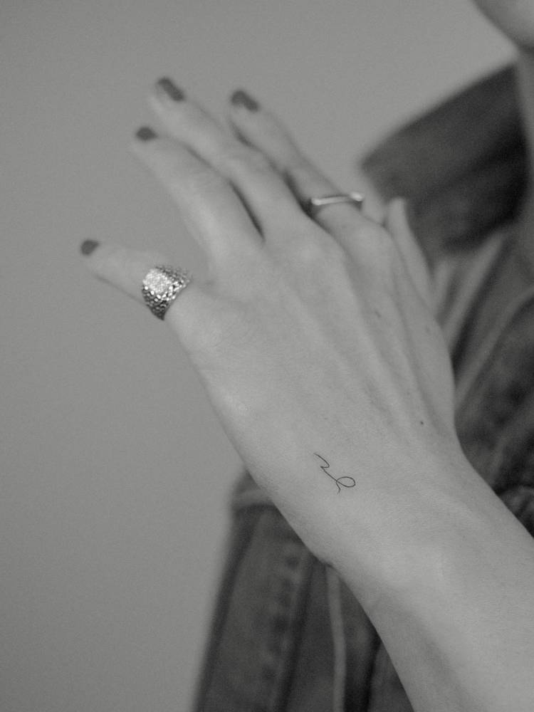 Tiny initials tattoo located on the hand, minimalistic style.