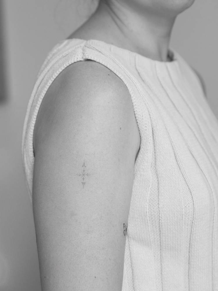 Fine line style little ornament tattoo located on the upper arm.