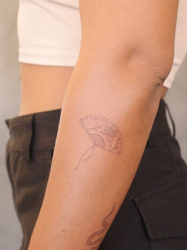 Hand fan in fine line style tattooed on the forearm.
