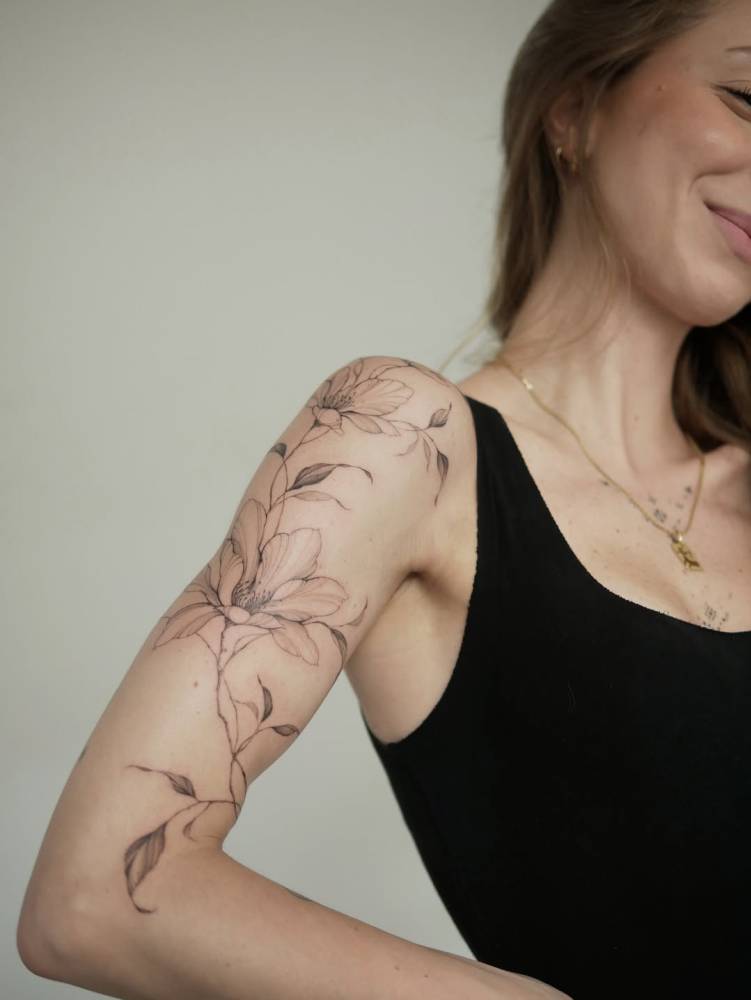 Illustrative style magnolias tattooed on the upper arm.