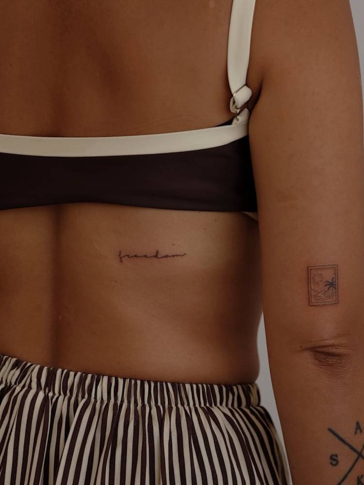 Handwritten font word "freedom" tattooed on the back.