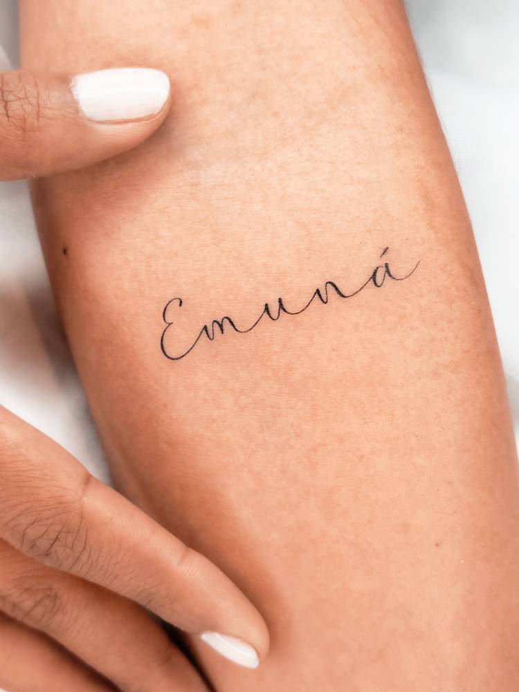 "Emuná" lettering tattoo located on the inner forearm.