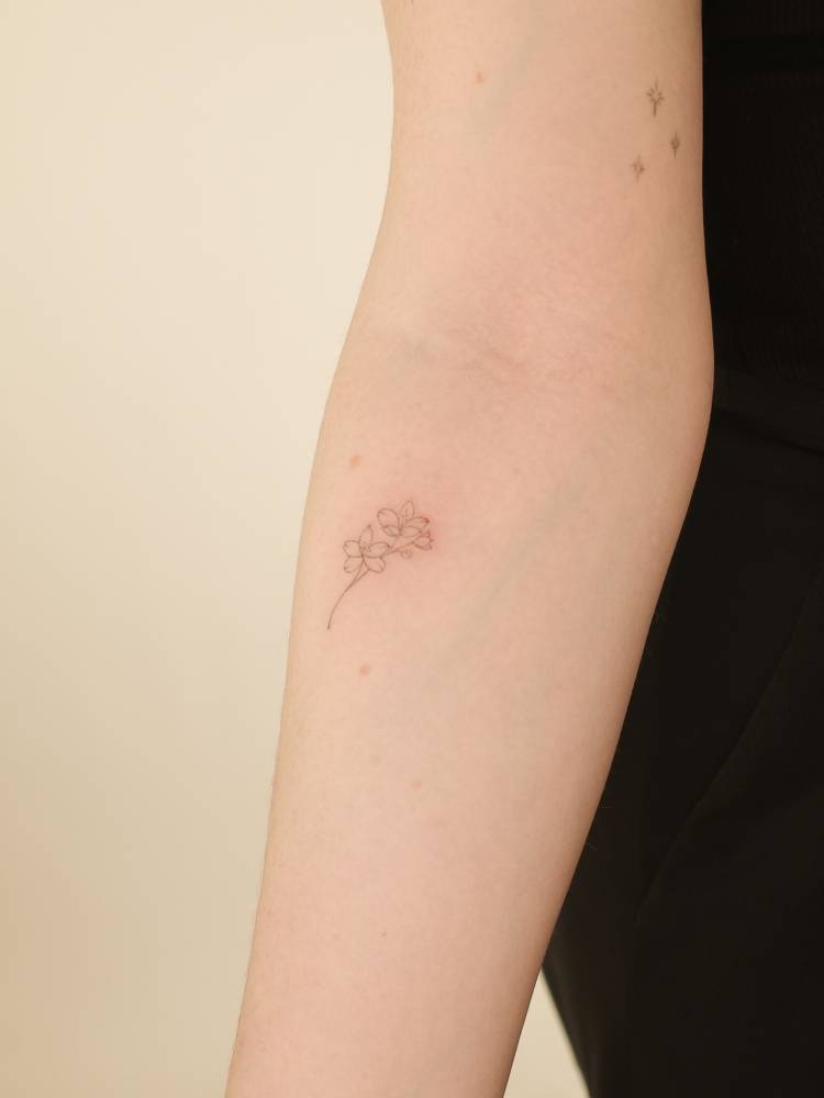 Tiny fine line style cherry blossom tattoo located on the inner forearm.