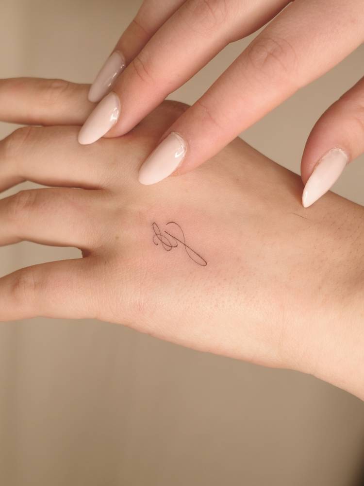 Script font letter "g" tattoo placed on the hand.