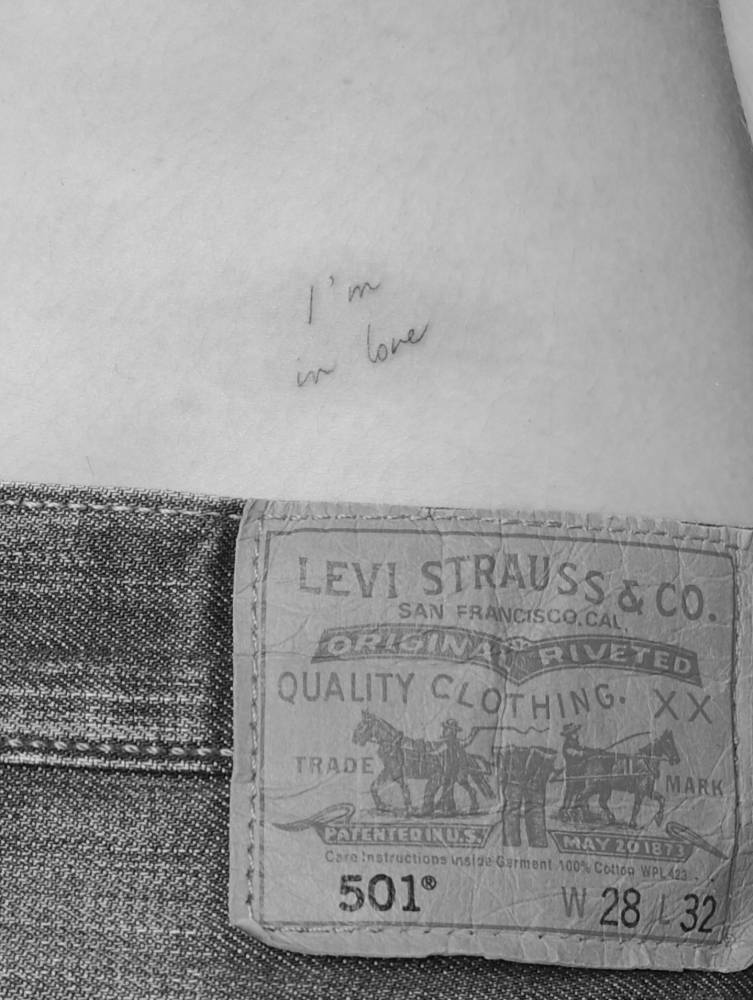 "I'm in love" lettering tattoo in handwritten font placed on the lower back.