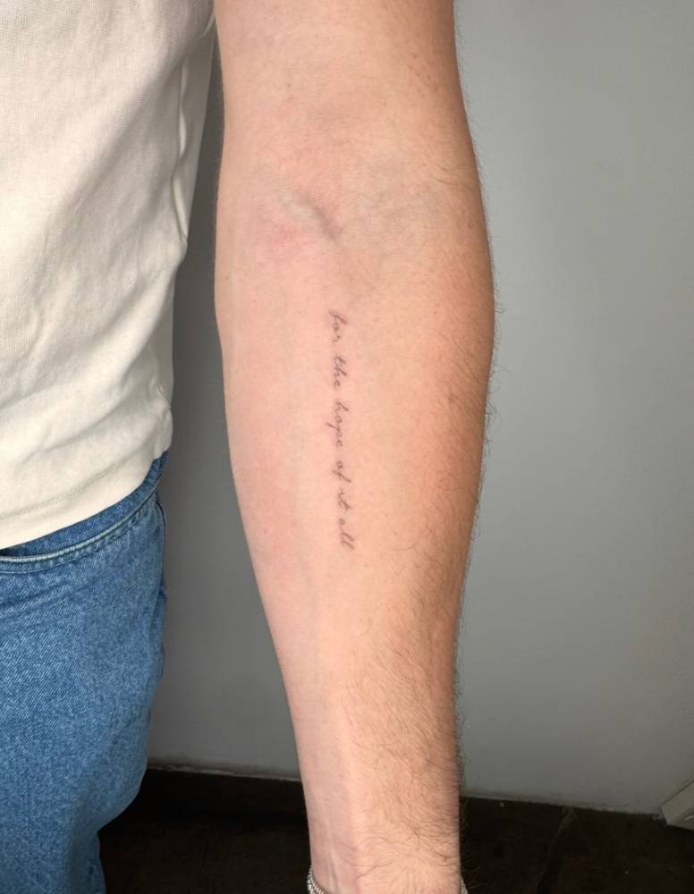 "For the hope of it all" lettering tattoo in handwritten font located on the inner forearm.