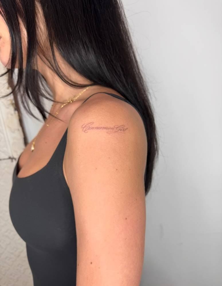 "Cinnamon girl" lettering tattoo located on the shoulder.