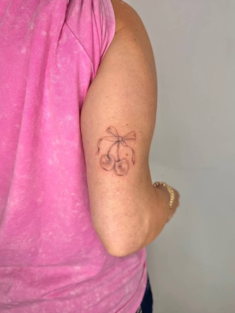 Cherries and bow tattoo located on the tricep, illustrative style.