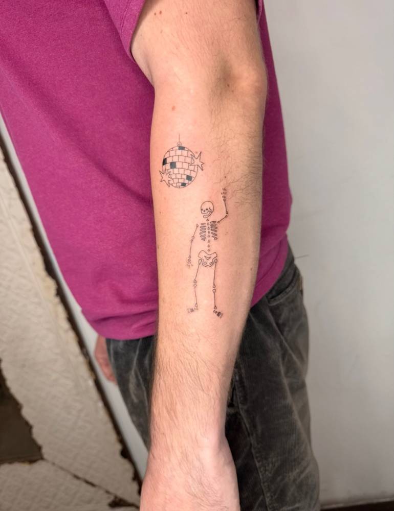 Fine line style skeleton and disco ball tattoo located on the forearm.