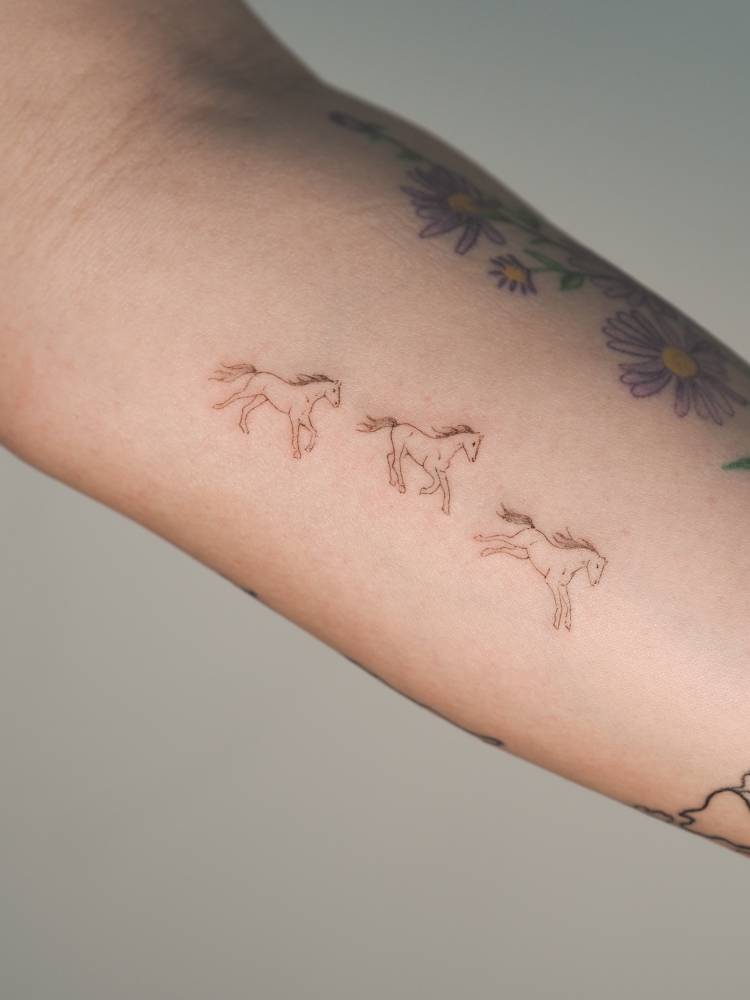 Three little horses in fine line style tattooed on the inner forearm.