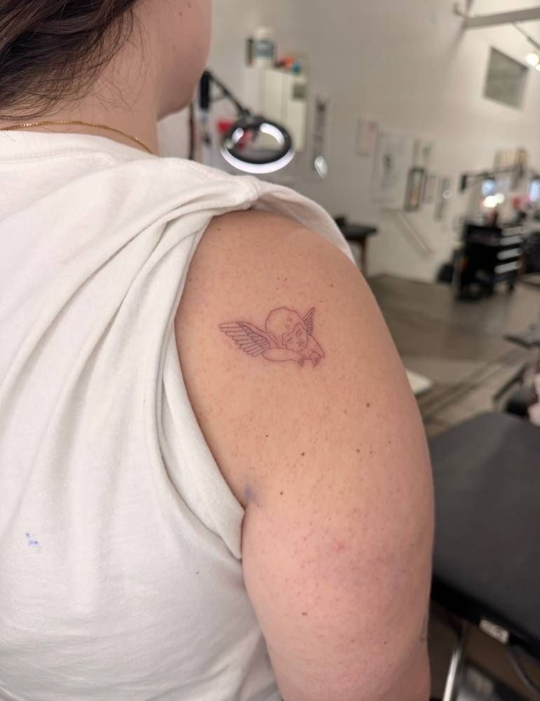 Sleeping cherub tattoo located on the shoulder, fine line style.
