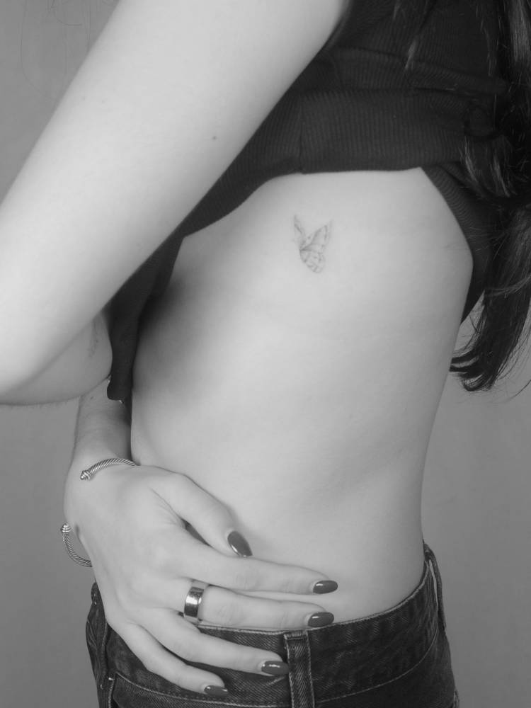 Butterfly tattoo in fine line style located on the side boob.