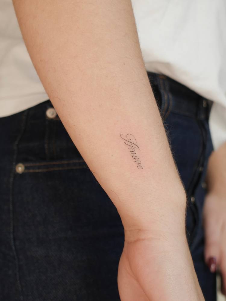 Script font word "amore" tattooed on the wrist.