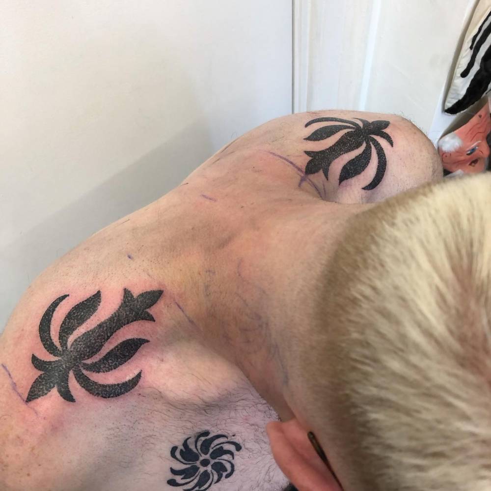 Individual matching hand poked ornaments tattooed on the top of shoulders.