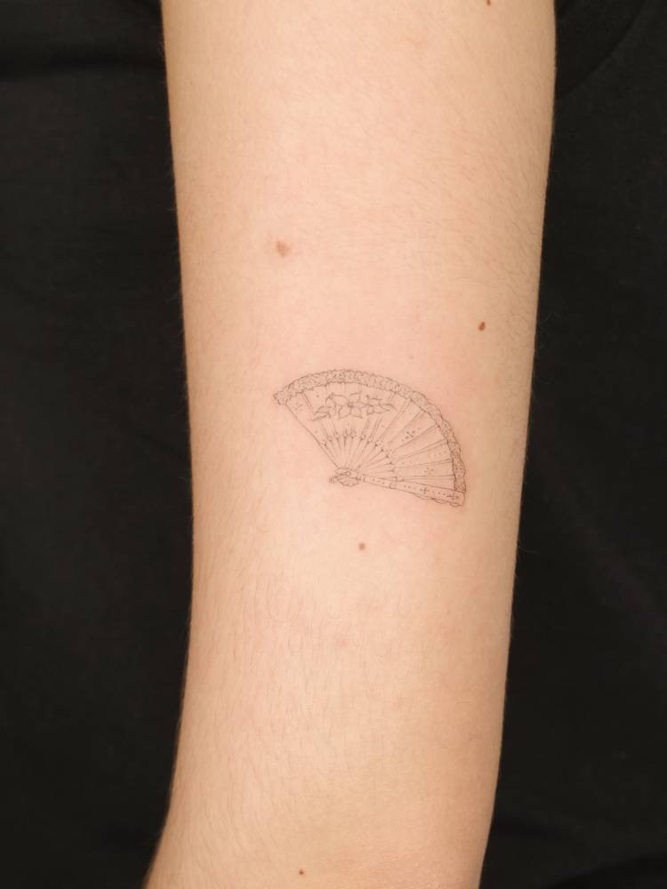 Hand fan tattoo in fine line style placed on the upper arm.