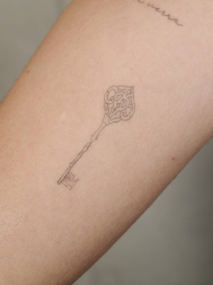 Key tattoo placed on the inner forearm, fine line style.