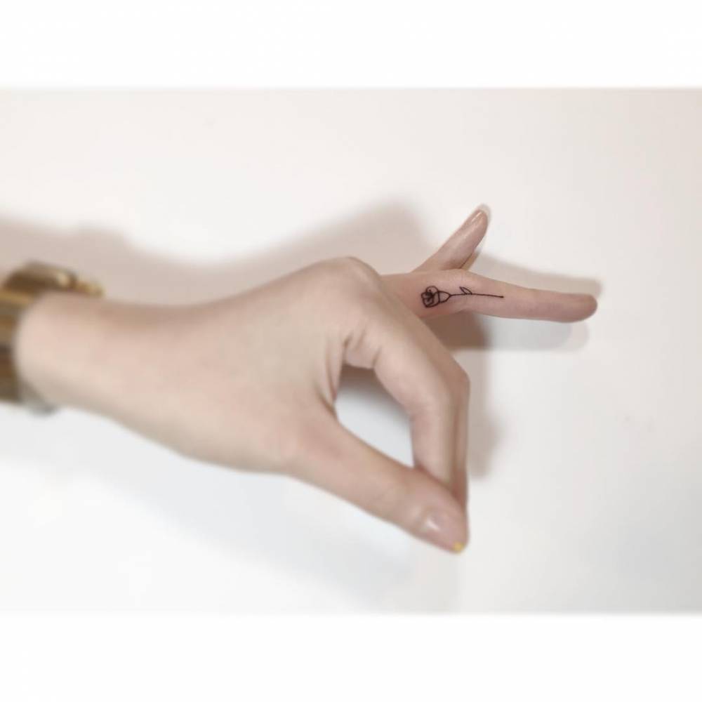 Tiny rose in fine line style tattooed on the finger.