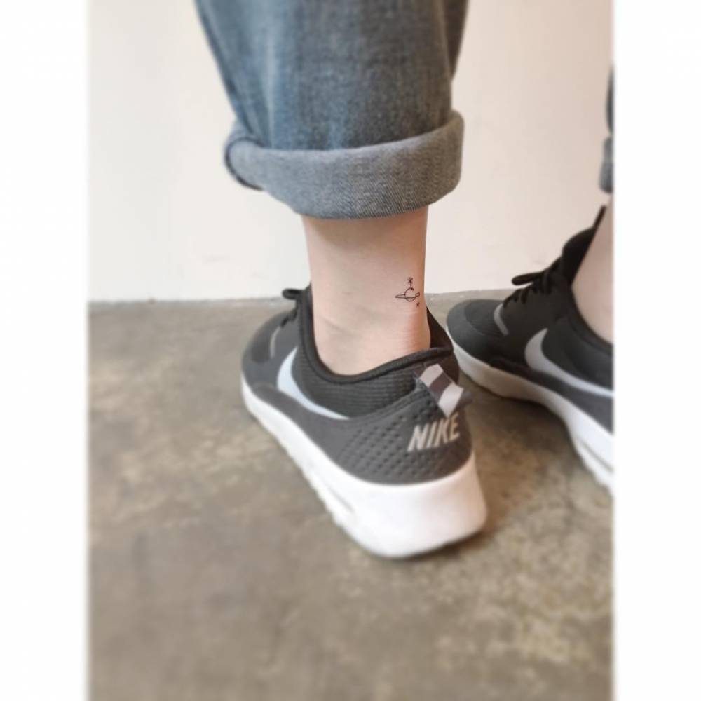 Tiny Saturn tattoo in minimalistic style located on the achilles.
