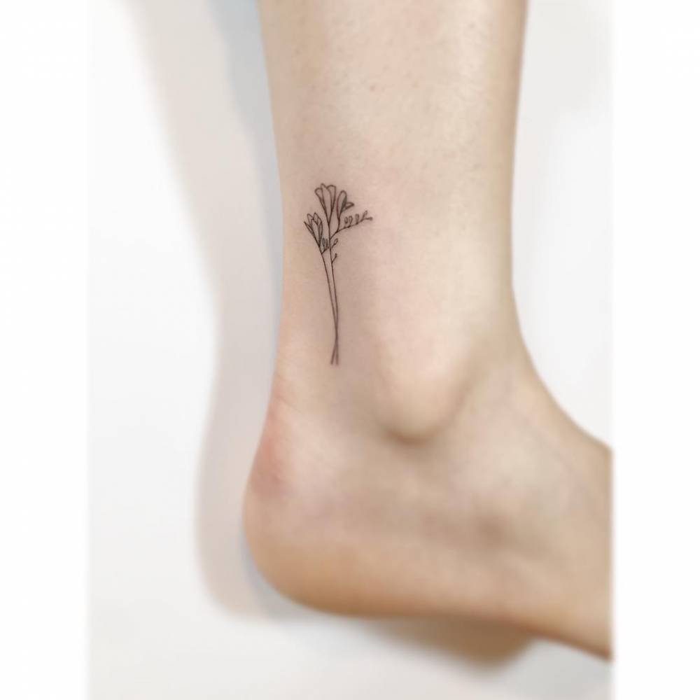 Freesia flower in fine line style tattooed on the ankle.