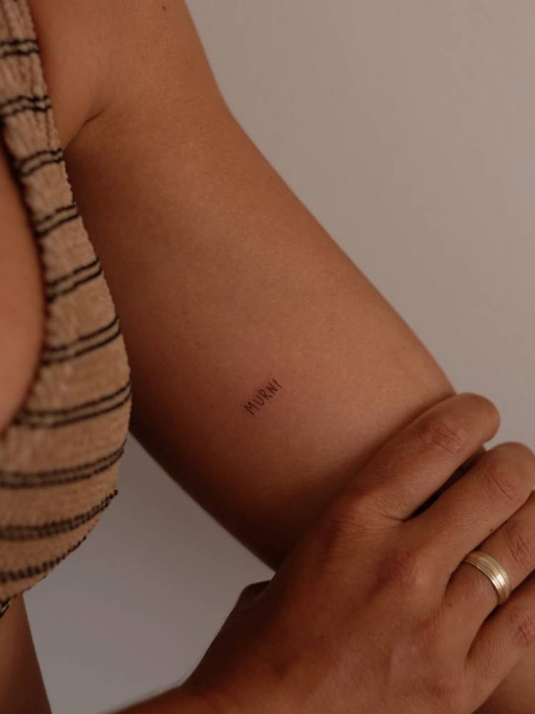 Handwritten font word "murni" tattooed on the inner arm.